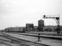 A general overview of Canadian Pacific's Guelph Junction is shown, looking west along the Galt Sub in August 1959. The caboose and tail-end of a westbound freight is visible, along with the westbound signals, water tower, and coal tower. The shop building is hidden in the background, and the station is out of view just to the right of the photo. The CP Goderich Sub to Hamilton (presently part of the Hamilton Sub) branches out at the bottom left, with the north portion of the Goderich Sub continuing to Guelph (the Guelph Junction Railway) and on to Goderich partially visible in the background on the right.