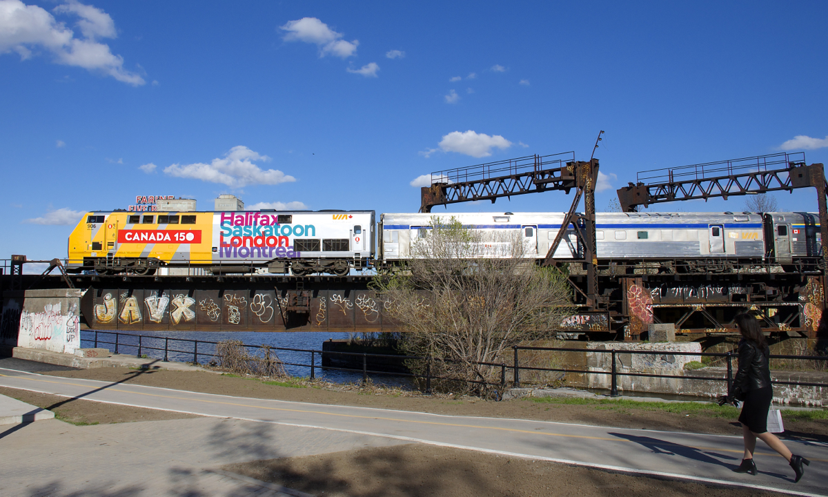 VIA 64 is nearly into Montreal's Central Station as it crosses the Lachine Canal at CN Wellington with VIA 906 leading. VIA 906 is wrapped for Canada's 150th anniversary and 4 cities served by VIA Rail are listed on each side.