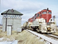 TH&B 73 and 402 are southbound on the Dunnville Subdivision with over 45 cars of phosphate rock for ERCO at Port Maitland. They are passing by Penn Central's 'E&O' interlocking tower as they clunk-clunk across the Canada Division mainline. PC employee, Operator/Leverman WA Webster has locked the armstrong levers into proper position to allow for this movement. The 3 wooden structures ( tower, outhouse and coal bin) are well weathered at this stage. 