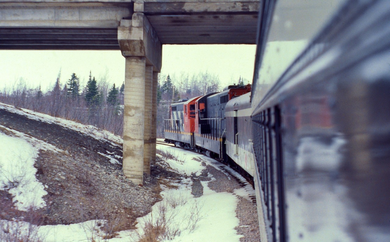 UNDER THE OVERPASS. Terra Transport Mixed Extra 935 West crosses under the TCH Overpass at Bishops Falls  shortly after leaving the station on April 16, 1988. This was the photographers's third trip on the mixed and the very first (and only) for his friend Paul. The two would be the only passengers for the entire 138 mile journey to Corner Brook with the exception of a lone cabin owner who boarded at Millertown Junction and departed at Gaff Topsail. A special treat for both riders was that the train left Bishops Falls with passenger only equipment (Baggage 1308 and Coach 764) and would remain a mini 'Caribou' until four container units were picked up in Grand Falls, thus making it a true mixed. With the completion of the Trans-Canada Highway in 1965, dozens of overpasses were constructed across the right of way throughout the Island but most, such as this one, have since been replaced with corrugated steel pipe to allow access for the Trans Canada Trail.
