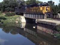 With leased GP38's reflecting in the water, Extra B&O 4806 West has descended the grade off the Cainsville Fill and is about to cross Locks Road in the southeast end of Brantford. This is where water collected in Mohawk Lake drains via a small damn into the Grand River. On this day the empty slab cars are right on the head end. You can visit this location via the Hamilton-Brantford Rail Trail,  which utilizes the TH&B right-of-way.