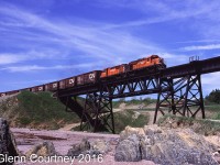 A pair of New Brunswick East Coast Railway head east along the Baie des Chaleur enroute to Gaspe with seven boxcars for copper anode loading. They will return in a few hours with copper anode loads. The bridge they are on is of course one of the many bridges on the line that lead to its current out of service condition. 