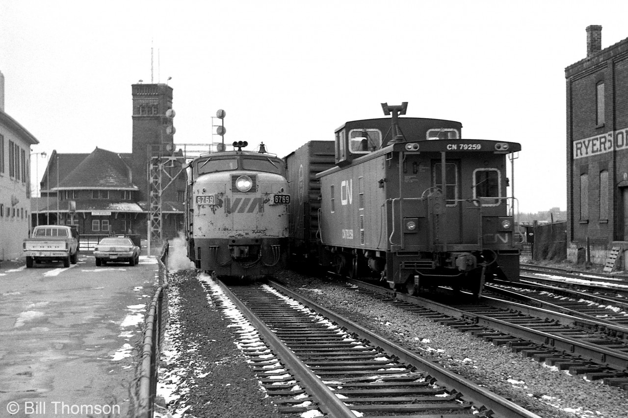 VIA #74 with FPA4 6769 in the lead departs Brantford Station eastbound, passing CN van 79259 on the tail end of a westbound freight in 1982.