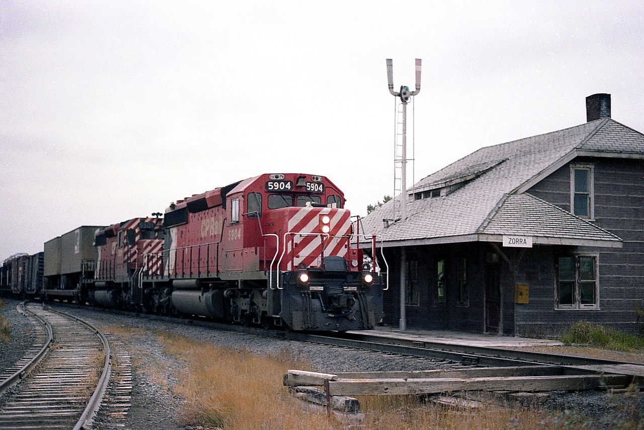 The old Zorra station has been gone a long time. The story I heard concerning it's demise was CP dug a big pit, broke down the structure and shoveled the remains into it. Quick and easy. This was once the junction of the Galt sub and the line from St. Marys thru to Ingersoll; the north portion removed 1995 and the south to Ingersoll in 1987. Eastbound mixed freight, led by CP 5904 and 5501 in an older paint scheme, has an interesting mix we do not see any more. Truck trailers on flat cars. Forty-foot boxcars, exposed auto cars, and so on. Pity it is such a dull day. The track on the left is the lead into the LaFarge (Canada Cement) plant behind me.