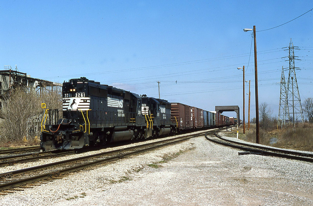 On Apr 30/85, Conrail operated the CASO for the final time. The next day CN and CP took title of the 225 or so miles of double track and sidings, yards etc.  Fast forward 2 years and CN has negotiated with Chessie ( almost  CSX) to have certain trains operate between their Chatham Sub and Fargo using trackage rights and 2 new connections. Since we’re still in the train order era, a new office was put into use named CN Chatham East. This was immediately south of the CN Chatham Sub and east of the C&O diamond, using an old connecting spur that once served Darling & Co ( renderings). On Apr 8/87, I caught NS train 327 as he passes through the truss bridge and beyond the Chatham East connecting track with SD40-2’s 3261-3313 (both delivered as Southern Rly when new) operating long hood forward. The new structure for the Chatham East operator is immediately behind me. The burnt remains of the former CIL fertilizer plant can easily be seen behind the bare trees/shrubs.