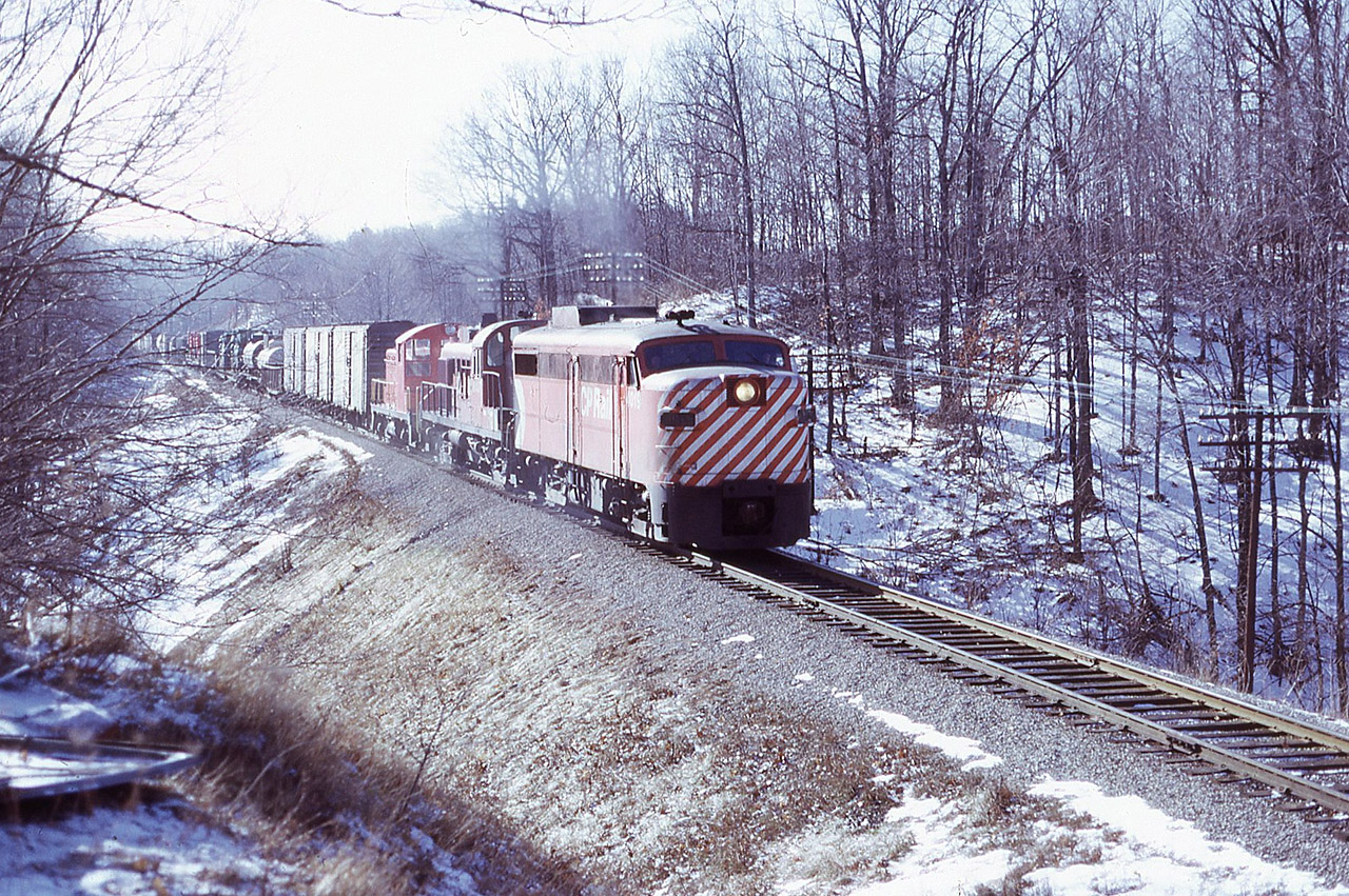 Approaching Waterdown is Extra 4019 North with RS-3 8437 and dead SW-1 IREX 5 ex Vermont Rly trailing ( for AA Merrilees at West Toronto). The Hamilton area phone lines were buzzing this day as the train was being marshalled at TH&B Aberdeen Yard. This would be today’s version of the Ham Turn. This shot was taken off the shoulder of Snake Road immediately south of the old overhead bridge ( which at that time was iron with wood planks). Needless to say he was working hard with a 46 car train which includes a couple of transformers from Westinghouse.
It was mid morning in January hence my tendency to over expose.