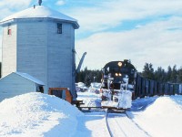 A typical winter afternoon, I was the headend brakeman on the Exeter Switcher and we paused at Lone Butte for a picture or two. The Exeter Switcher did the bulk of work at Exeter (100 Mile House) switching several sawmills, plywood plant, bulk oil spur as well as other smaller customer trackage. After those chores were completed, we head south and switched several mills along the way. Quite often we ran as far south as Lime siding and switched the copper ore loading ramp and cement silos. We were a "full crew", Conductor, Engineer and two Brakemen. It was a long day working, quite often on duty 14 or 16 hours. Our home base on this job was Exeter Two crews worked this assignment in Exeter, each crew working 3 days and then 4 days off. Pay wise it was lucrative, but, the four days off was the real incentive.
The old water tower was a reminder of the days of steam. The tower is still there, a group of local residents have taken on the preservation. Lone Butte was a time table "additional flag stop" for the passenger train.
as a footnote, this slide is part of Bruce Mercer collection