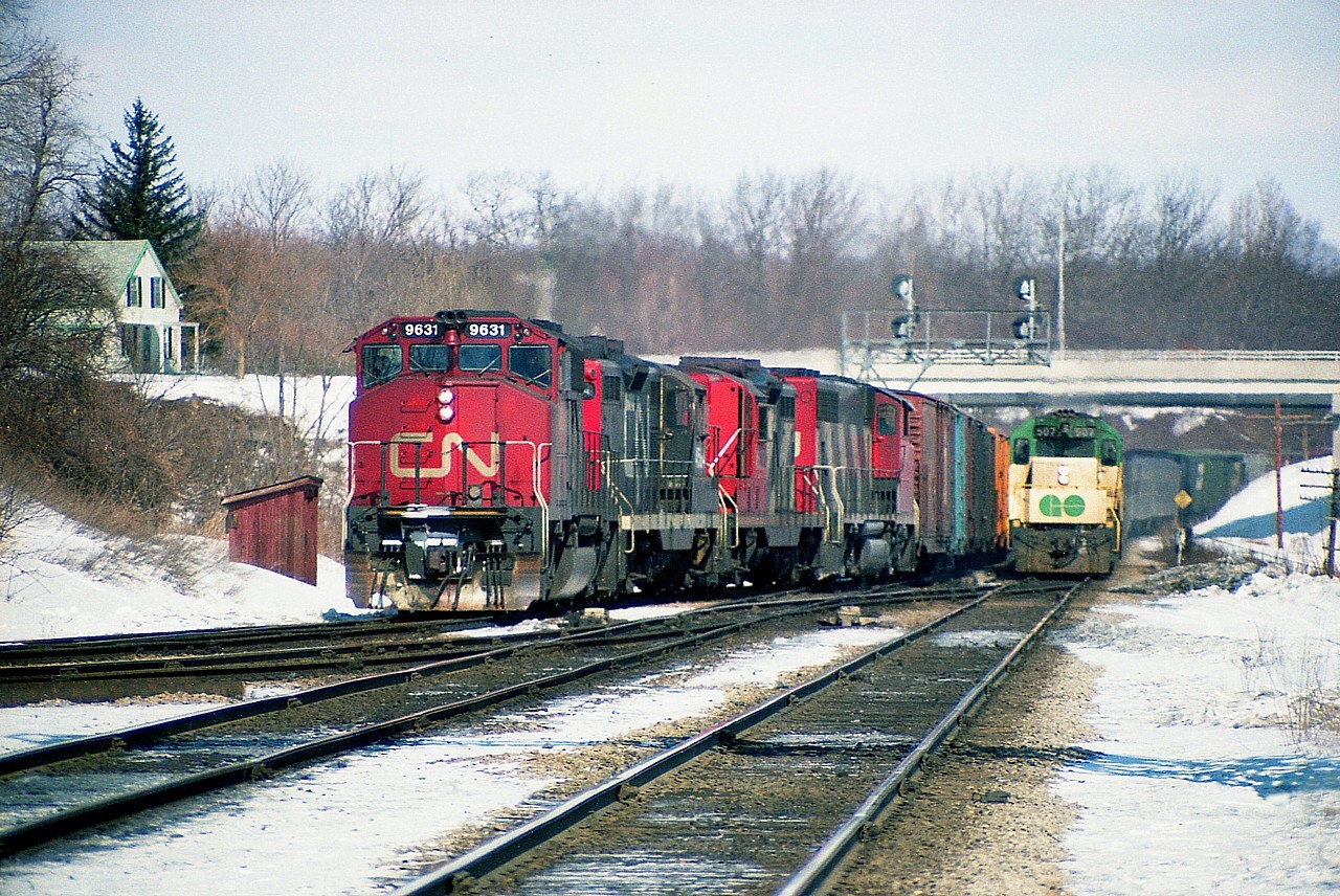 GO 507 is temporarily on CN passenger service as train #73 races westward alongside a freight about to head up the Dundas sub. The passenger is pulling 9 coaches; the freight, behind CN 9631, 4584, 4536 and 9647 according to my notes are 87 cars and caboose 79568 in tow. Nobody out on the walkbridge this day; and interesting to note how wide open the "railfan house" is back then. We used to comment on being the owner of that house if it ever came up for sale.