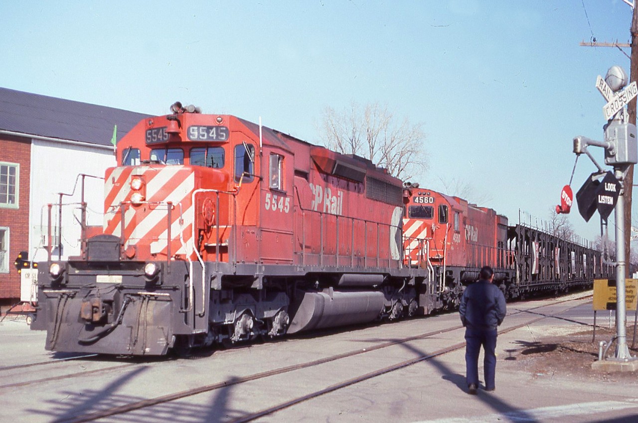 A westbound with 1 green flag passes through Chatham on the CP Windsor Sub on Feb 23/84 with 5545-4560 doing the honours. I had positioned myself at this particular crossing (the name of which I forget) with the sole intention of having a train pass by the wigwags. Unfortunately one of the locals came walking up just as the train arrived. I believe thats a Marathon Realty sign behind the crossing signal pole.