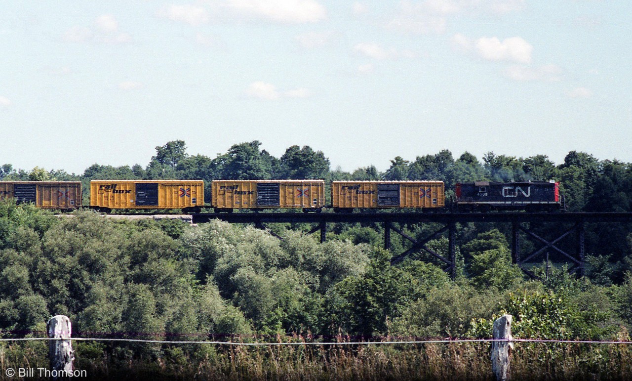 Further to the photo of CN 4508 switching the yard at Alymer, the wayfreight is shown here before arrival in town, crossing a bridge on the line to the west. In tow behind the GP9 are then-modern yellow Railbox boxcars, one slightly fresher/newer than the others.