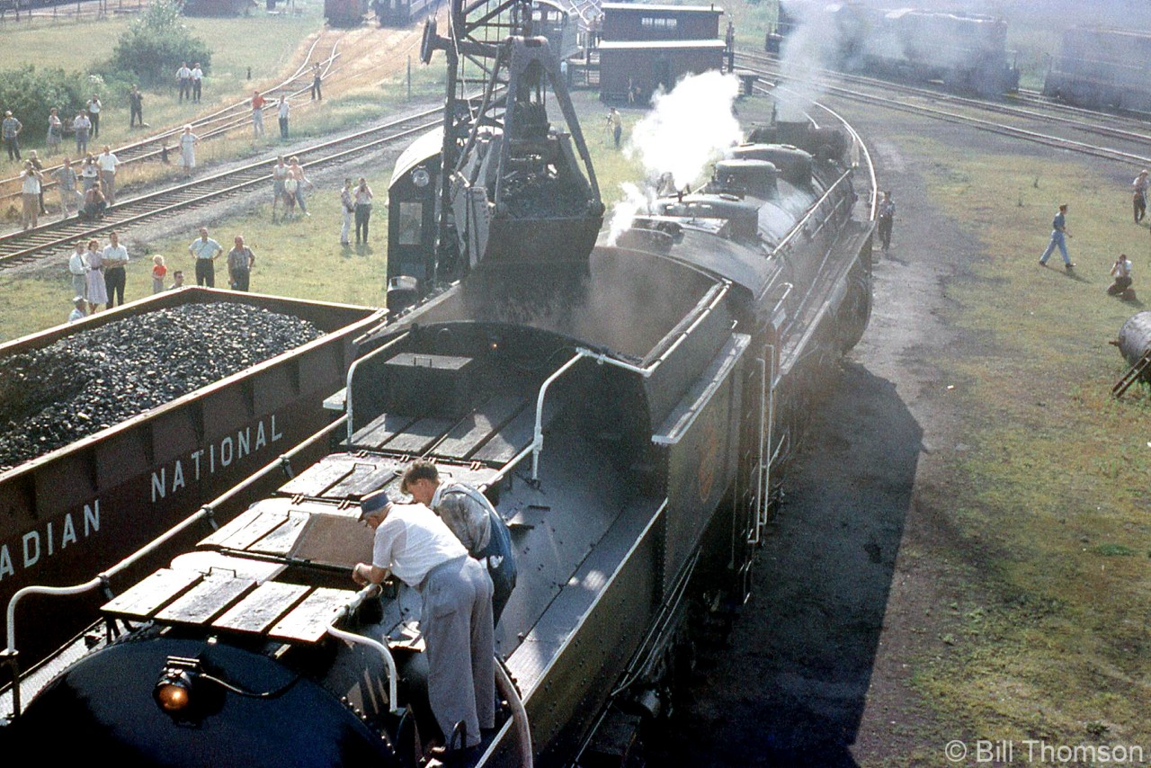 Another view of Canadian National's Northern 6167 getting refueled at Niagara Falls during the July 10th 1960 URCS fantrip, taking in all the action from a higher vantage point: crew members on her tender attend to her water needs, as CN crane 50018 dumps another clamshell load of coal into her tender from a hopper car positioned adjacent. Railfans and fantrip attendees around the shop grounds observe and photograph the action, amid first generation diesel units crowding the shop tracks.

From the same fantrip:
Ground view at Niagara Falls: http://www.railpictures.ca/?attachment_id=29331
Taking on water at Port Colborne: http://www.railpictures.ca/?attachment_id=29510