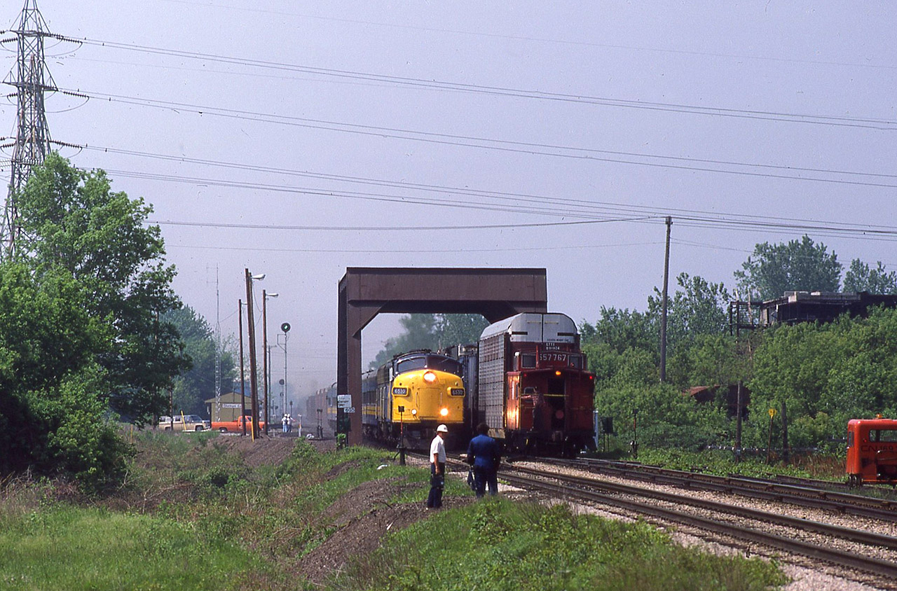 See http://www.railpictures.ca/?attachment_id=29360 for the related, and immediate prior image.
NS train 27 and VIA 74 are passing each other on the McGregor Creek through truss span while some engineering employees are discussing and inspecting the on-going project. Train 27 has a pair of C30-7's while F9's 6530-6632 are coming at me, having made the station stop just moments earlier. The dust being kicked up from both trains is not necessarily indicative of their speed; rather it is from trackwork that was done to install the connector so that CN trains can use C&O Subdivision 2 between here and Fargo, and further use the Caso Sub to Windsor and beyond.
In a couple of years, NS will revamp their service and renumbered trains 343/344 will begin using this connector and hence the Detroit River tunnel (after the ferries are removed). The speeder adds a nice touch to this scene. The high green signal on the left is the train order light for CN Chatham East. The burned and abandoned former CIL fertilizer plant is slowly disappearing in the foliage. The tan coloured pickup truck at the office belongs to Operator Fletcher who was Ken Annett's father-in-law.