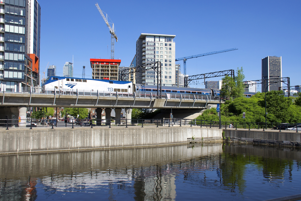 AMTK 113 backs the deadheading Adirondack past Montreal's crane-filled skyline on a sunny morning.