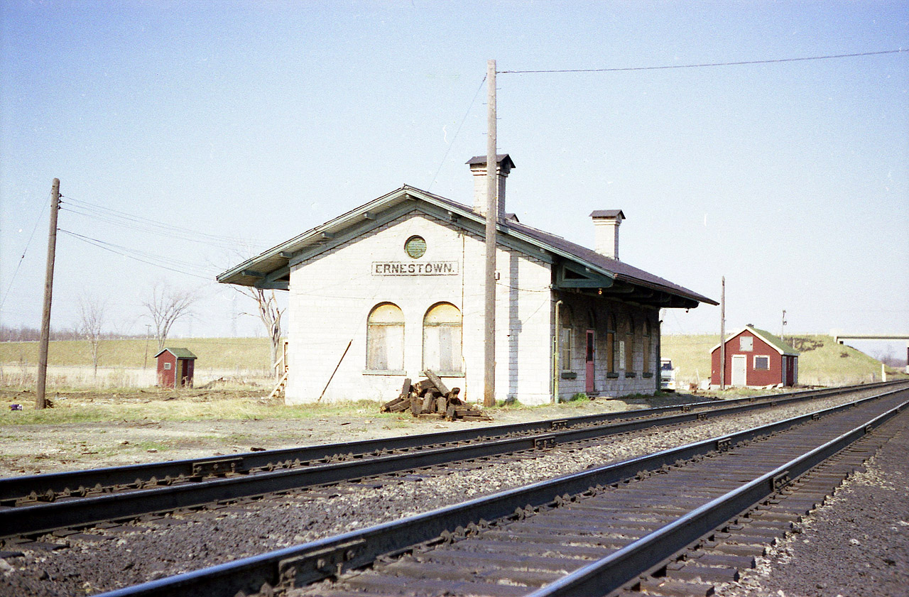 Ernestown is not much of a place. Never was, never will be. This station, built way back in 1855, was actually built to serve the town of Bath, about 5 KMs away. Passenger service was always light; but trains have not stopped here since the 1950s, and for a while MoW used specially-built rooms in this building. That lasted up to about 1990, and by that time all out-buildings had been razed. That includes the Hi-Visibility Outhouse behind the station. The stone building is now protected under the Heritage Act, as of 1994. It was one of around 30 stations of it's type that once stood in Ontario; but now we are down to just a few: others include Port Hope, Prescott and St. Marys' Jct. Photographic opportunity here not as wide open as it once was; trees have encroached on the scene.