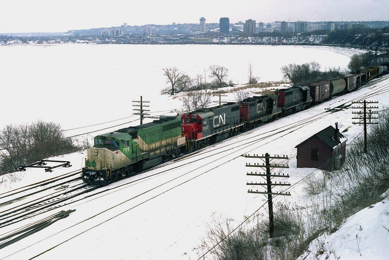 Although it may not look it, this was one of the coldest days I ever experienced out there waiting for a chance to shoot a passing train. I was standing out in the elements with Bill McArthur, and we went so far as to try and get out of the stiff wind off the frozen harbour by standing behind trees about six inches thick. :o) The temperature was somewhere between 6 and 12F. And a strong wind. Of course we knew the train would take its' time in Hamilton yard, and of course we knew there was a GO leader. It was probably a half hour before it passed by our numb shutter-fingers, on its way to Toronto. GO 709, CN 5502, 4525 and 50xx the power. Decent reward for our patience, although I thought we were positively nuts at the time.