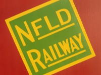 AVONDALE ARTWORK. The green and yellow tilted wafer of the former Newfoundland Railway has been accurately recreated on ex-CN Tool and Office Work Car 5015. Originally built as CNR RPO 1803 by CC&F in 1952, it was converted to work service after the end of RPO service in October 1968. Today the tilted wafer adorns this beautifully restored car as NR RPO 233 in its resplendent red and black livery on display near the oldest wooden station in Newfoundland at Avondale.   