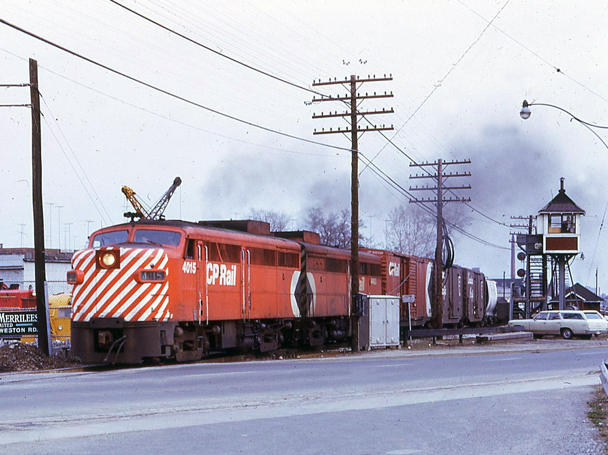 CP train 955 headed up by an FA-1/FB-1 combo of 4015-4405 charges around the connecting track off the North Toronto Sub. and onto the Mactier Sub. In the left background is the small yard of Andrew Merrilees where red SW1 IREX 5 is resting. This was formerly Vermont Railway No. 5 and a former Erie Lackawanna unit before being sold to the equipment dealer. The CN crossing watchman’s tower is protecting traffic on Old Weston Road, and the watchman's little white dog seems to be inspecting the movement of 955 from the top step ! I was working 2nd trick at CN West Toronto and at the approach of each train, if possible, I would stand in the parking lot with my camera.