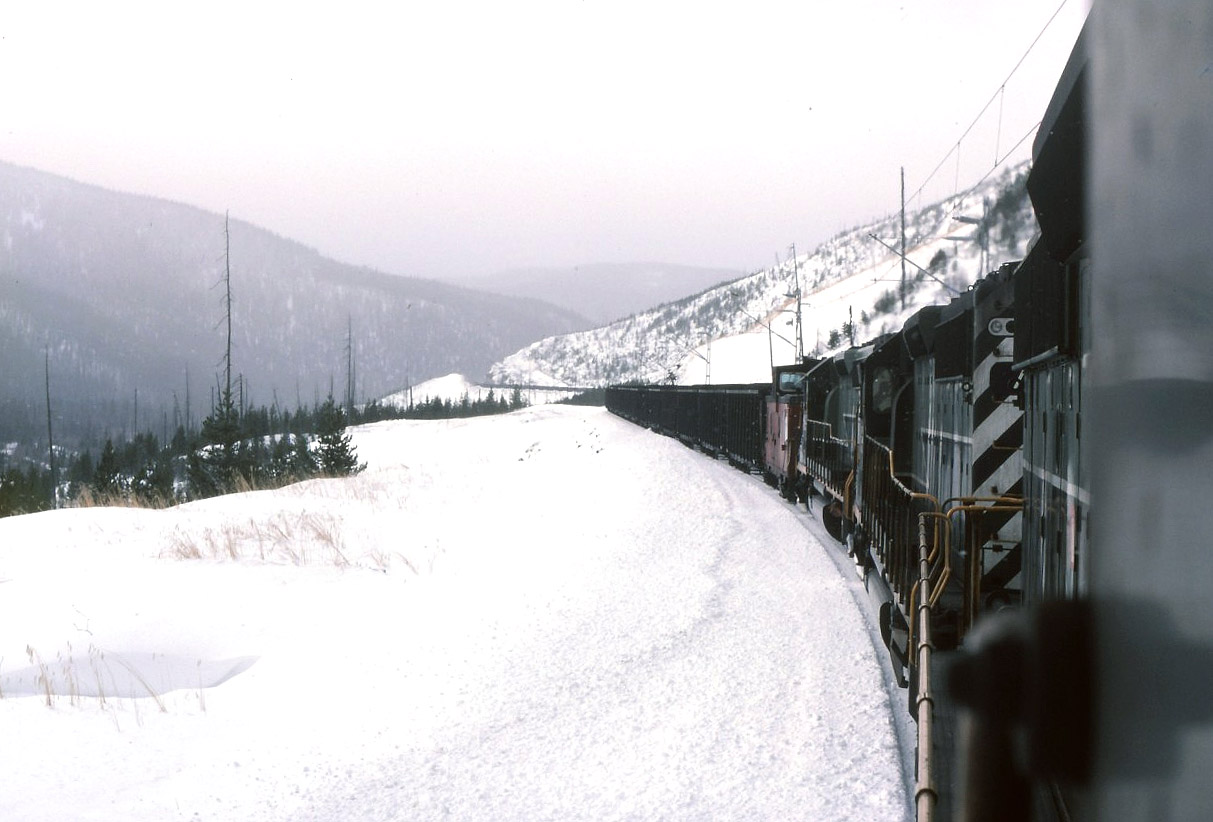 My view from pusher power assisting a south bound coal train "up the mountain" on a bleak winter afternoon. About center of the image you can see the train snaking through a rock cut, the lead power is beyond that point. If I recall, at the time most coal trains were 98 loads. We pushed on the caboose that had strengthen frames etc for coal service. The crew members would ride one of the pusher units instead of the caboose as per railway requirements for safety. The three SD40-2's that we had were in run 8 for most of the time grinding up the hill. It could get quite gassy and poor air in the Wolverine tunnel particularly if the leading power was diesels. If all the units were electric the air quality was good in the tunnel.