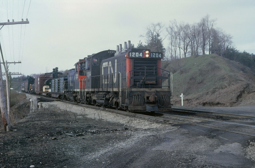 The good old days at Bayview Jct, you could drive right in, stay as long as wanted and take pictures. Image taken here on a overcast spring morning of a switcher job leaving Hamilton and heading east to somewhere. With two units back to back and sequenced numbers 1204 & 1205. Not sure of the train designation or where they were going. Had some loads of electrical equipment, most likley from Westinghouse. Also there was some type of passenger coach near the tailend, not sure if I got a picture nor what the car was.
