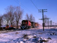 A cool shot on a bitterly cold day finds CP westbound time freight 917 with 5750- QNSL 208 (being purchased by CP) making a small setoff at Chatham.
There was an expression used by C&O workers, that on cold winter days when the snow is dry, it " runs " as the wind pushes it from one place to another. This was in reference to otherwise flat terrain where the snow would 'run' and accumulate to the lee of a hedgerow or a stand of trees. Such is the case on this bright morning, as 917 appears to be moving at track speed. In fact, the head-end man has made the cut on the Chatham cars and they are pulling ahead to clear the plant, in order to get the rail & signal to shove the cars into the yard. The caboose was probably being changed out for the Chatham-based roadswitcher.