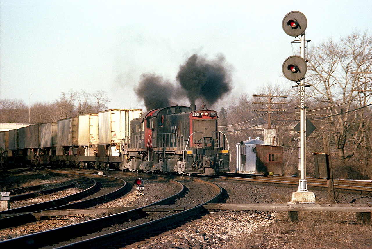 Classic MLW power!!!  Old CN S-13 switchers 300 and 303 accelerate thru Bayview Junction on their way to the Hamilton TOFC facilities in this somewhat rare image. Built in 1959, they were renumbered from 8600 series. The 300 was formerly 8600 and in 1985 became 8710. The 303 was previously 8603 and it did not face renumbering again, but rather was retired in 1989. Units of this series were seen regularly around Spadina, shuffling passenger cars and consists, but on freight service such as this they proved to me very difficult to catch. I recall them around Hamilton only briefly early in 1980.