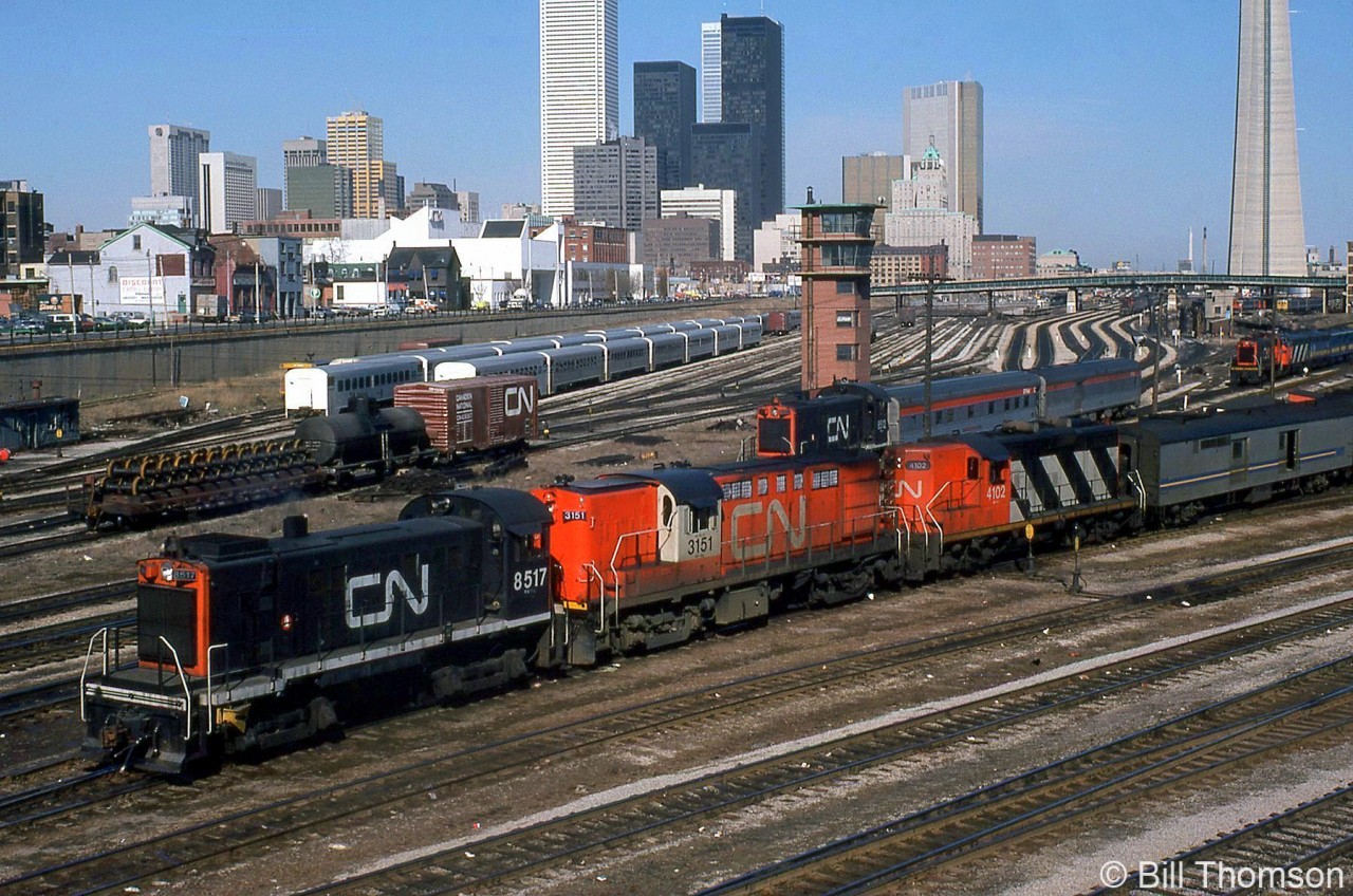 The view from downtown Toronto's Bathurst Street bridge in April 1979 shows a flurry of action: CN S13 switchers were still switching complete passenger trains (coaches & locomotives) between Union Station and the Spadina coachyard and nearby roundhouse/shop facilities. CN S13 8517 handles a Tempo train consist with RS18 3151 and GP9 4102, while sister 8512 handles a pair of ex-CP Stainless Steel Budd cars, by now owned by VIA but still in CP colours. In the background another S13 can be seen coupled to a train with FP9-F9B power in the coachyard, and in the distance another S13 can be seen handling a passenger train under Spadina Avenue bridge. RDC cars at Spadina roundhouse are visible at the base of the CN Tower on the right, and GO Hawker Siddeley single-level commuter coaches can be seen stored on the left at Bathurst North Yard, which appears to still be partially in use as a freight yard.

More at Bathurst Street:
VIA's The Canadian: http://www.railpictures.ca/?attachment_id=22282
Steam era switching: http://www.railpictures.ca/?attachment_id=15641
Up close S13 view: http://www.railpictures.ca/?attachment_id=27375
RDC's departing on #663: http://www.railpictures.ca/?attachment_id=20820