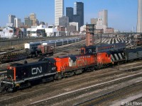The view from downtown Toronto's Bathurst Street bridge in April 1979 shows a flurry of action: CN S13 switchers were still switching complete passenger trains (coaches & locomotives) between Union Station and the Spadina coachyard and nearby roundhouse/shop facilities. CN S13 8517 handles a Tempo train consist with RS18 3151 and GP9 4102, while sister 8512 handles a pair of ex-CP Stainless Steel Budd cars, by now owned by VIA but still in CP colours. In the background another S13 can be seen coupled to a train with FP9-F9B power in the coachyard, and in the distance another S13 can be seen handling a passenger train under Spadina Avenue bridge. RDC cars at Spadina roundhouse are visible at the base of the CN Tower on the right, and GO Hawker Siddeley single-level commuter coaches can be seen stored on the left at Bathurst North Yard, which appears to still be partially in use as a freight yard.
<br><br>
<b><i>More at Bathurst Street:</b></i><br>
VIA's The Canadian: <a href=http://www.railpictures.ca/?attachment_id=22282><b>http://www.railpictures.ca/?attachment_id=22282</b></a><br>
Steam era switching: <a href=http://www.railpictures.ca/?attachment_id=15641><b>http://www.railpictures.ca/?attachment_id=15641</b></a><br>
Up close S13 view: <a href=http://www.railpictures.ca/?attachment_id=27375><b>http://www.railpictures.ca/?attachment_id=27375</b></a><br>
RDC's departing on #663: <a href=http://www.railpictures.ca/?attachment_id=20820><b>http://www.railpictures.ca/?attachment_id=20820</b></a>