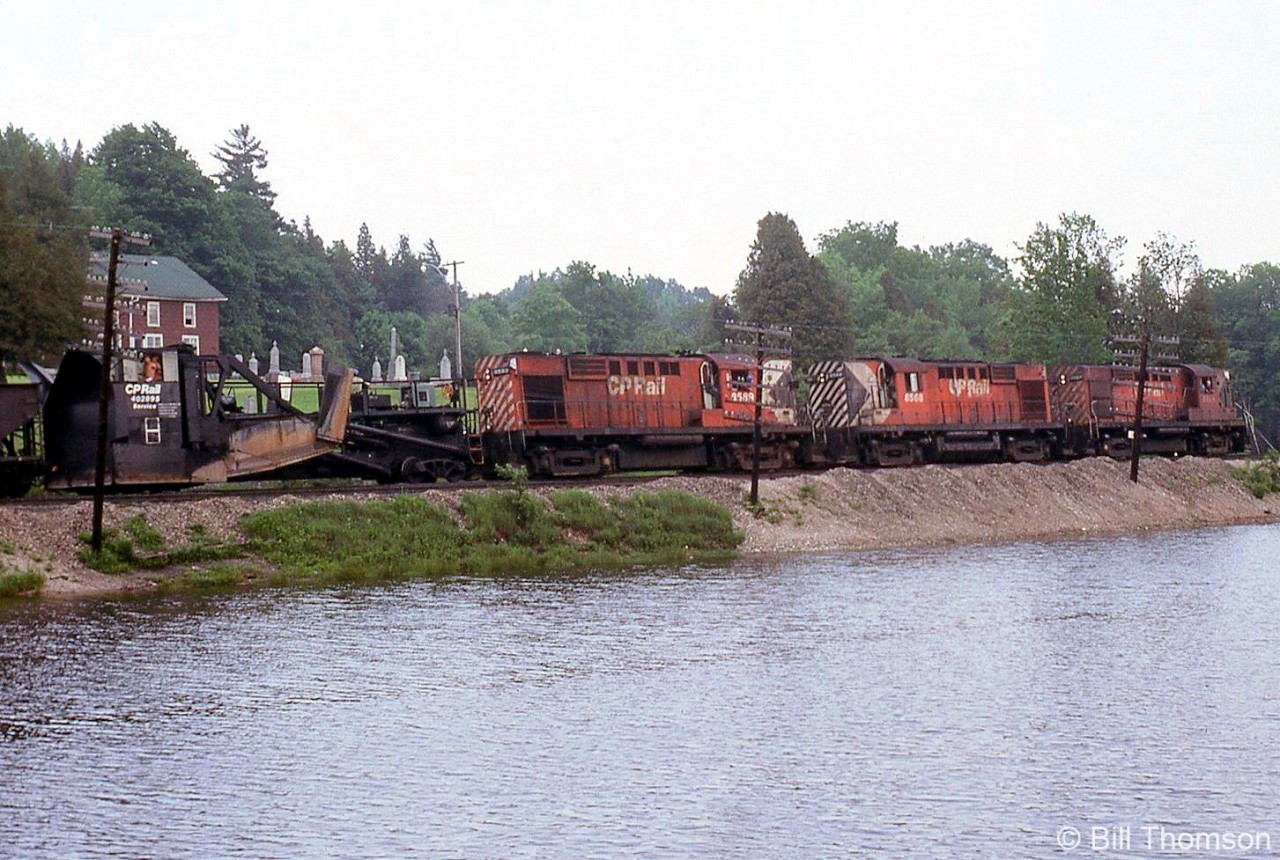 A CP Rail ballast train led by MLW RS10's 8584, 8568, & 8599 rolls past the pond at Campbellville with Jordan spreader 402895 marshalled behind the power, on CP's Galt Sub on June 7th 1979.Typically used in winter service clearing mainlines, branchlines, yard tracks and sidings, in the warmer months Jordan spreaders were put to use on ballast trains spreading track ballast (typically done by more modern maintenance equipment today).