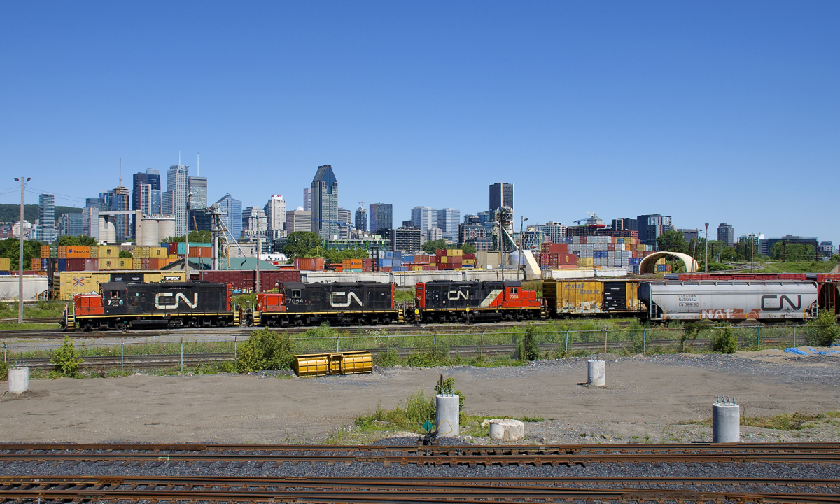 A trio of GP9's (CN 7226, CN 7054 & CN 7083) are switching Pointe St-Charles Yard. Behind them is the Montreal Sub and behind that is the skyline of downtown Montreal. In front of them are tracks leading to the AMT Pointe-Saint-Charles Maintenance Centre. This is the view from a new park that overlooks the yard just west of it, along Sebastopol Street.