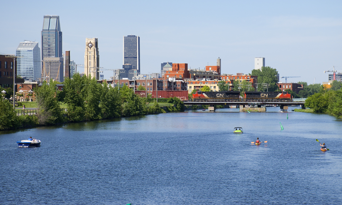 CN 2873 and CN 3039 lead CN 324 over Lachine Canal on a warm afternoon in Montreal, with the downtown skyline in the background and a number of boaters out on the canal.