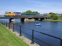 VIA 67 has LRC cars in three paint schemes and wrapped VIA 6436 leading as it crosses the Lachine Canal, with a pleasure boat passing at right.