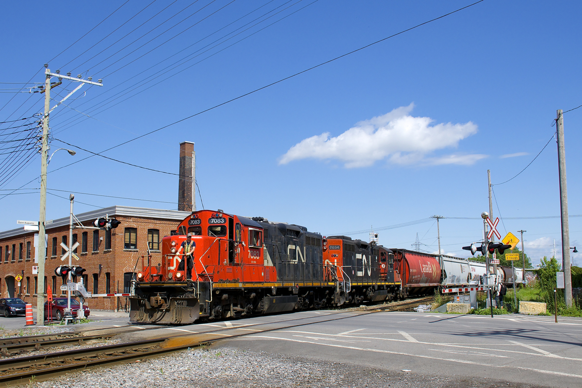 CN 7083 & CN 7054 are heading west on the north track of the Montreal Sub as they cross St-Ambroise Street. Soon they will back up on the East Side Canal Bank Spur and drop off eight cars at the Robin Hood Flour Mill.