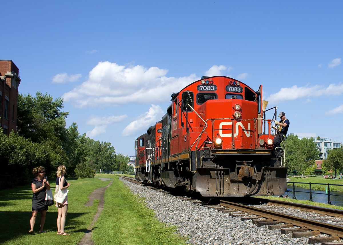 Two women stop and watch as CN 7083 & CN 7054 head light on the East Side Canal Bank Spur after dropping off eight cars at the Robin Hood Flour Mill (the last client on this line). At right is the Lachine Canal.