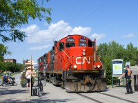 A crewmember is flagging a pedestrian crossing beside the Atwater Market as a pair of GP9's (CN 7083 & CN 7054) head light on the East Side Canal Bank Spur after dropping off eight cars at the Robin Hood Flour Mill (the last client on this line).