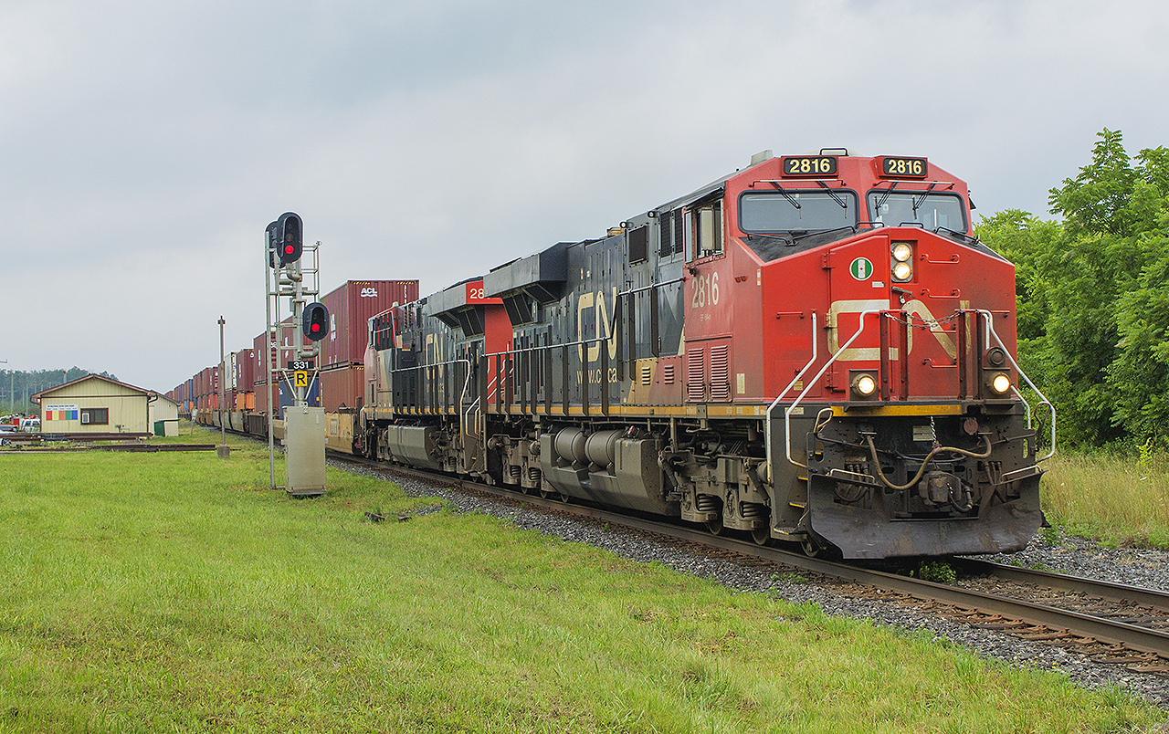 Like many of the smaller communities along the Canadian Nationals Strathroy Subdivision, Watford has not changed much through the years. Having boasted one of the larger stations at one time, it was demolished as the railway did not wish to continue the maintenance of the building. With all passenger traffic being swirched over to VIA Rail, they started to build smaller, less attractive 'stations' along their corridors. Here, we see the Chicago to Toronto container train passing the current CN maintenance office. Of note, is the light standard just to the left of the signals. That remains from one of those small VIA shelter that existed until the early to mid 2000's before it too was demolished, probably due to low ridership. A similar structure still exists to the west in Wyoming.