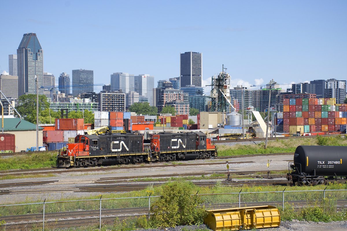 CN 7054 & CN 7032 are seen light in Pointe St-Charles Yard as they switch cars around with part of Montreal's skyline visible in the background.