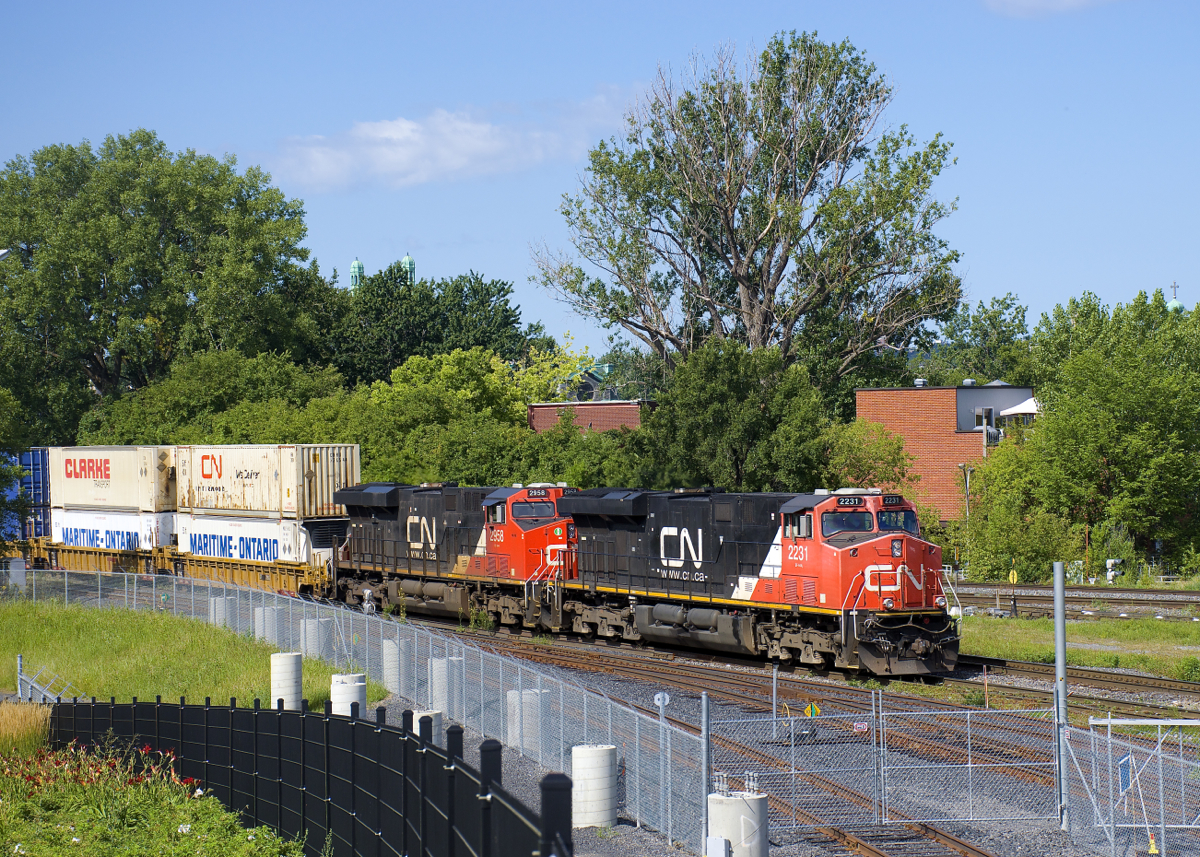 As seen from Montreal's new railfans park by Pointe St-Charles yard, CN 120 passes the entrance to the RTM's maintenance centre, with CN 2231 & CN 2958 up front.