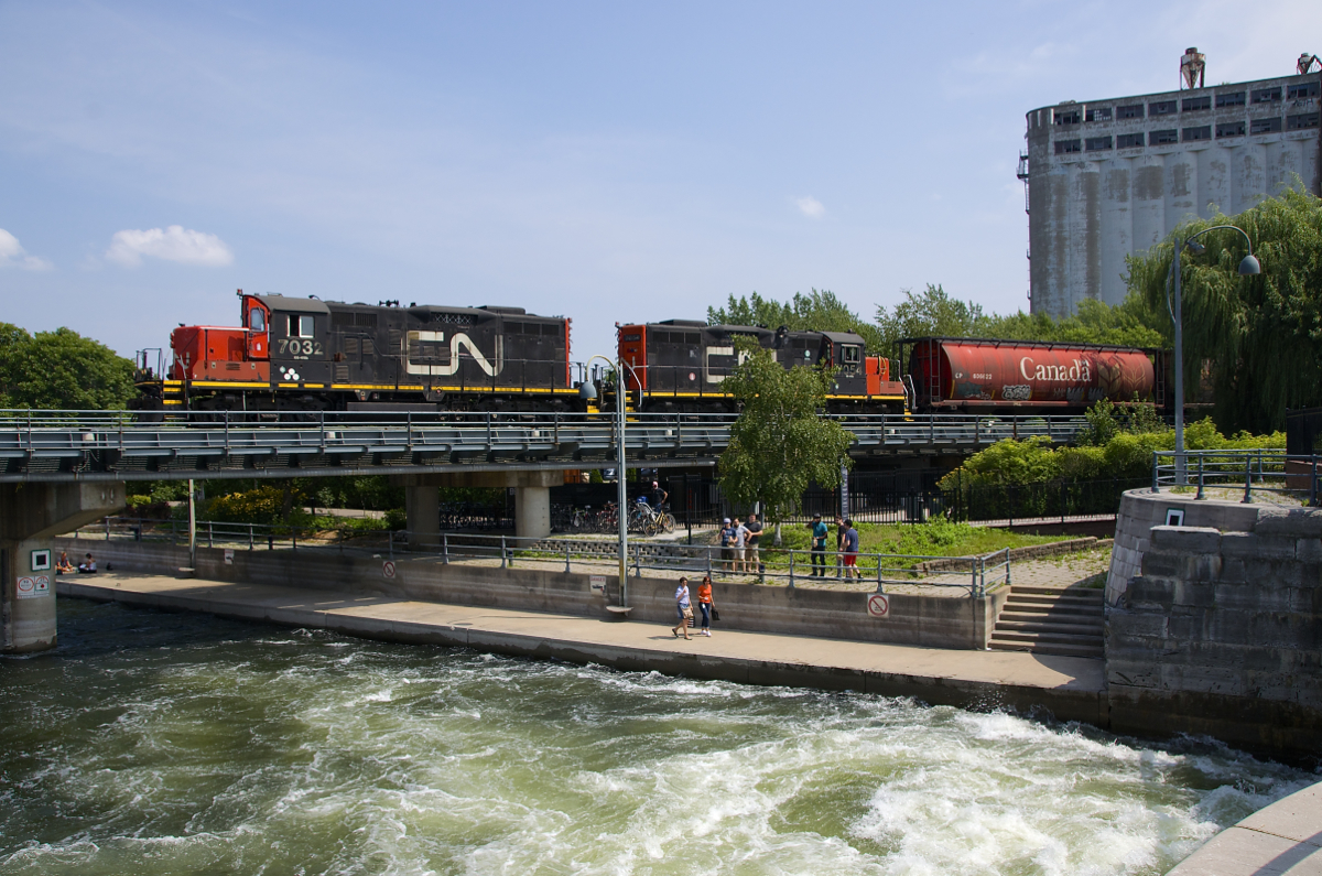 A pair of CN GP9's (CN 7032 & CN 7054) are stopped over the eastern end of the Lachine Canal before backing up with a cut of grain cars. The water is swirling underneath as a lock is opened.