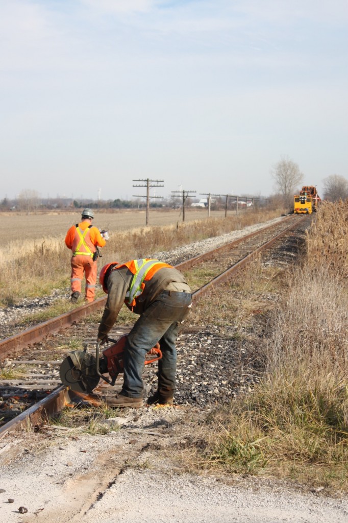 "Severing history" this was a sad day for me. I set my sights on the old CN CASO Subdivision east of Essex. I knew the rail train should be working somewhere that way and exited highway 401 at Tilbury and started checking most crossing west of their in hopes of catching the train. Just west of South Woodslee I finally located the train and it was a slow day of trying to get shots at a few crossings and across farm fields before the long drive back to Milton and that nights, night shift. The long trip rewarded me with a few good shots of something I would never get to do again. Shooting a train on the middle section of the CASO. Once such a mighty railroad with lots of history, today just a fading memory. Here we see one of the track crew cutting the rails at the Lakeshore Road 219 crossing, next the spike pullers will move in before the rail is lifted into place on the rail train. The rail here was apparently reused on a line out in western Canada.