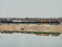 ONR's Englehart to Noranda train passes the Macassa Mine tailings disposal pond on the west side of the City of Kirkland Lake. Power this day is ONR 1731, 1800 and 1809. Many years ago tailings were pumped directly into this 'lake', but those days are gone and in this view we can see cleanup of the now disused pond under way. The water is being pumped out, the pond is isolated and being filled in as it was rather deep. The pump can be seen, as well as heavy equipment brought in to gently slope the shoreline as the pond is gradually eliminated. On the other side of this bridge is the kirkland lake itself. By the looks of google maps it appears not very much is left but green algae and sludge in the remaining pond. The train shown is a daily, at least back then, it ran to Noranda leaving Englehart early morning 0600 and returning there around 2100. Last time I saw it, 10 years back, power was one or two SD75I units depending on tonnage..