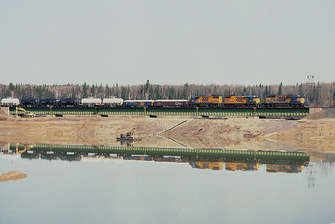 ONR's Englehart to Noranda train passes the Macassa Mine tailings disposal pond on the west side of the City of Kirkland Lake. Power this day is ONR 1731, 1800 and 1809. Many years ago tailings were pumped directly into this 'lake', but those days are gone and in this view we can see cleanup of the now disused pond under way. The water is being pumped out, the pond is isolated and being filled in as it was rather deep. The pump can be seen, as well as heavy equipment brought in to gently slope the shoreline as the pond is gradually eliminated. On the other side of this bridge is the kirkland lake itself. By the looks of google maps it appears not very much is left but green algae and sludge in the remaining pond. The train shown is a daily, at least back then, it ran to Noranda leaving Englehart early morning 0600 and returning there around 2100. Last time I saw it, 10 years back, power was one or two SD75I units depending on tonnage..