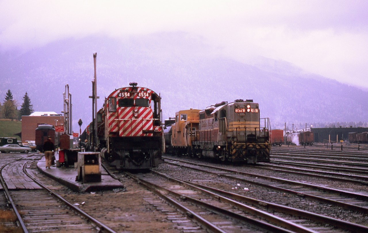 An MLW idles adjacent to the Revelstoke BC station during a crew change.  Meanwhile a GP works the rear of an eastbound.  Note the office car on the track to the left.  The station accommodated dispatchers and still served CP's Canadian.