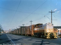 One from the slide collection: Canadian Pacific 6584, an MLW S3, operates on the Toronto Harbour Commissions' streetrunning trackage along Queen's Quay near York Street, hauling a sizeable cut of 40' boxcars. Judging from what appears to be ripped grain doors, they are likely grain empties being handled from one of the harbourfront elevators, such as Victory Mills in the background. According to <a href=http://www.trainweb.org/oldtimetrains/CPR_Toronto/WHARF.htm><b>Old Time Trains</b></a>, Toronto-based unit 6584 was unique as it outfitted with dual controls for easier rearward operation when switching Victory Mills' tight trackage on the East Wharf Job out of Parkdale Yard, which is likely its assignment here. The two sets of track to the left of the train were for TTC streetcars coming off Bay and heading to Harbour Loop, which were removed around mid-late 1965. <br><br> Long a source of traffic for the railways, as the downtown Toronto waterfront gentrified and lost much of its heavy industry, the railways too retracted. Most of the grain elevators on the waterfront shut down or were demolished, and the main streetrunning section here (known as the Central Harbour Terminals - Hanlan's Point District in employee timetables) was removed in the mid-80's, still leaving some trackage at the east end to service customers such as Redpath Sugar. The last of CP's ancient MLW switchers maintained out of John St. Roundhouse were retired around that time too, followed by John St. itself being closed by CP (although, happily, donated to the city for preservation). <br><br> <i>Duplicate Al Chione slide (although I'm not entirely sure if it was duplicated from another photographer's slide by him), Dan Dell'Unto collection.</i>