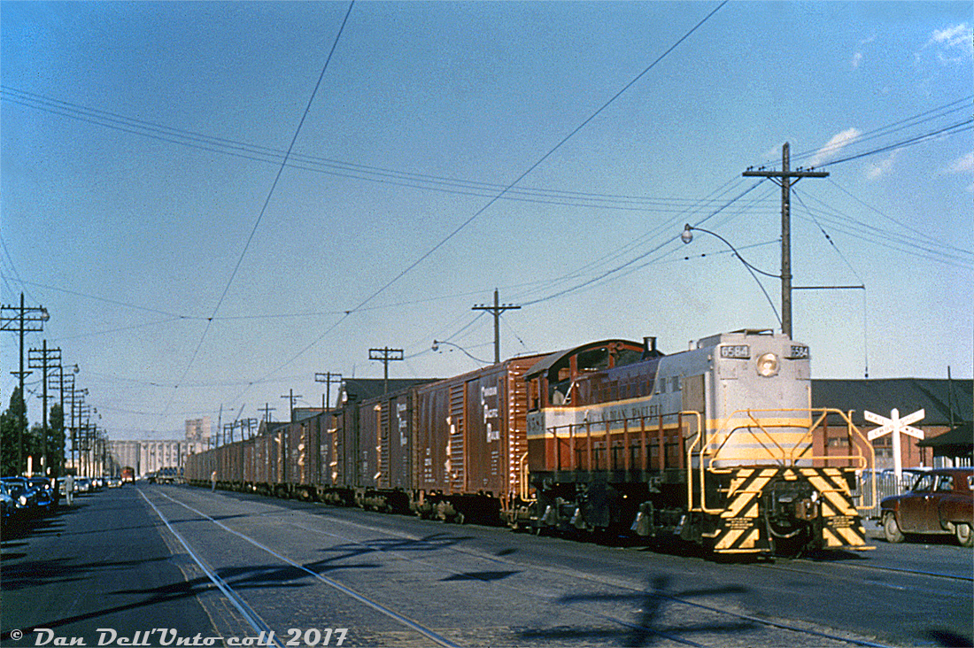 One from the slide collection: Canadian Pacific 6584, an MLW S3, operates on the Toronto Harbour Commissions' streetrunning trackage along Queen's Quay near York Street, hauling a sizeable cut of 40' boxcars. Judging from what appears to be ripped grain doors, they are likely grain empties being handled from one of the harbourfront elevators, such as Victory Mills in the background. According to Old Time Trains, Toronto-based unit 6584 was unique as it outfitted with dual controls for easier rearward operation when switching Victory Mills' tight trackage on the East Wharf Job out of Parkdale Yard, which is likely its assignment here. The two sets of track to the left of the train were for TTC streetcars coming off Bay and heading to Harbour Loop, which were removed around mid-late 1965.  Long a source of traffic for the railways, as the downtown Toronto waterfront gentrified and lost much of its heavy industry, the railways too retracted. Most of the grain elevators on the waterfront shut down or were demolished, and the main streetrunning section here (known as the Central Harbour Terminals - Hanlan's Point District in employee timetables) was removed in the mid-80's, still leaving some trackage at the east end to service customers such as Redpath Sugar. The last of CP's ancient MLW switchers maintained out of John St. Roundhouse were retired around that time too, followed by John St. itself being closed by CP (although, happily, donated to the city for preservation).  Duplicate Al Chione slide (although I'm not entirely sure if it was duplicated from another photographer's slide by him), Dan Dell'Unto collection.