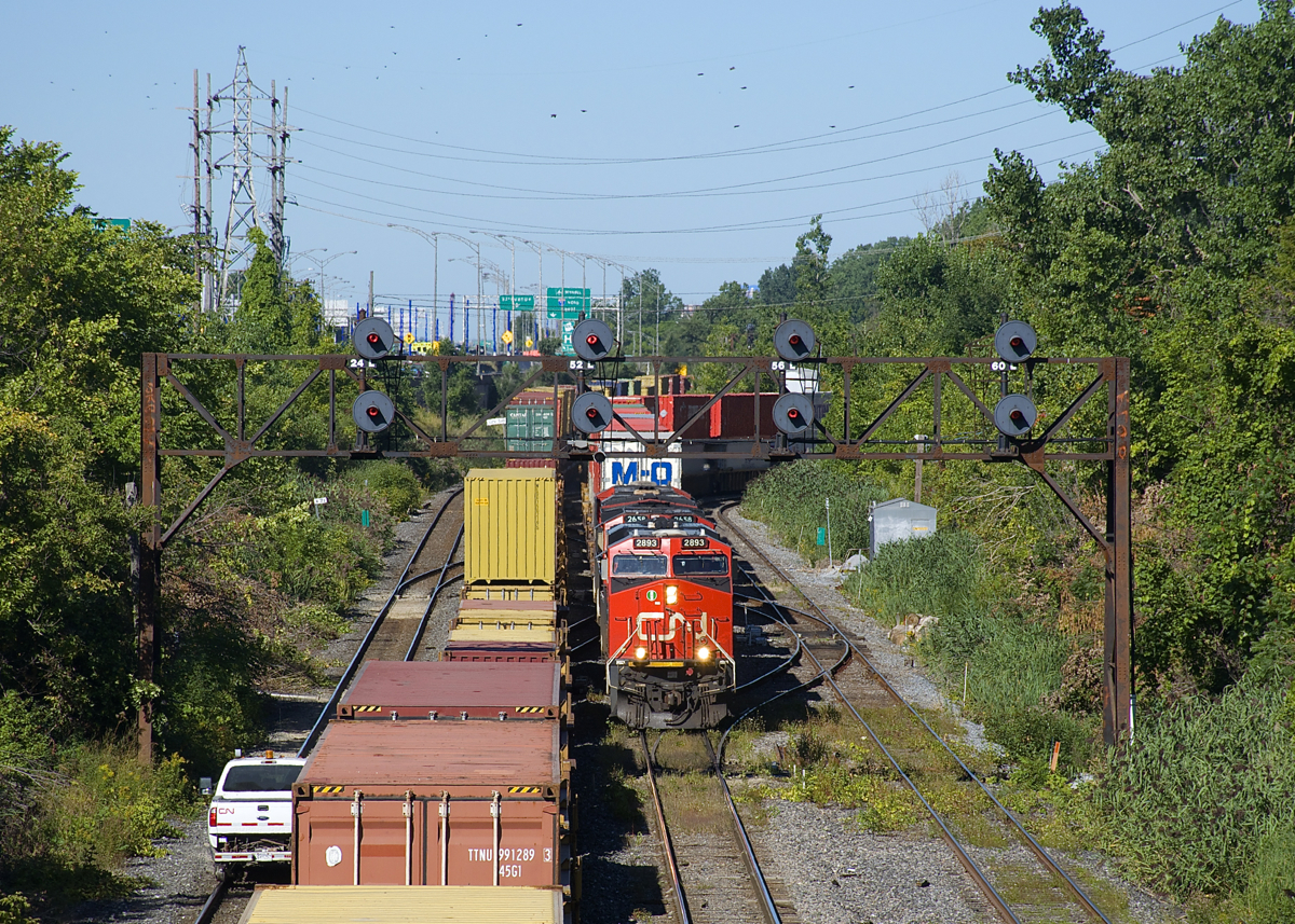 CN 120 (with CN 2893, CN 2658 & CN 2956 up front and CN 2858 mid-train) is exiting Taschereau Yard on the freight track, just as CN 149 is passing on the north track. The south track is also occupied, with a hi-railer stopped.