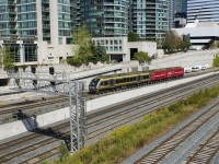 A Union Pearson Express shuttle train has just left Union Station in downtown Toronto, en route to Toronto Pearson International Airport as it approaches the Spadina overpass. The second car is a 'wrap' sponsored by the CIBC bank celebrating Canada's 150th anniversary.