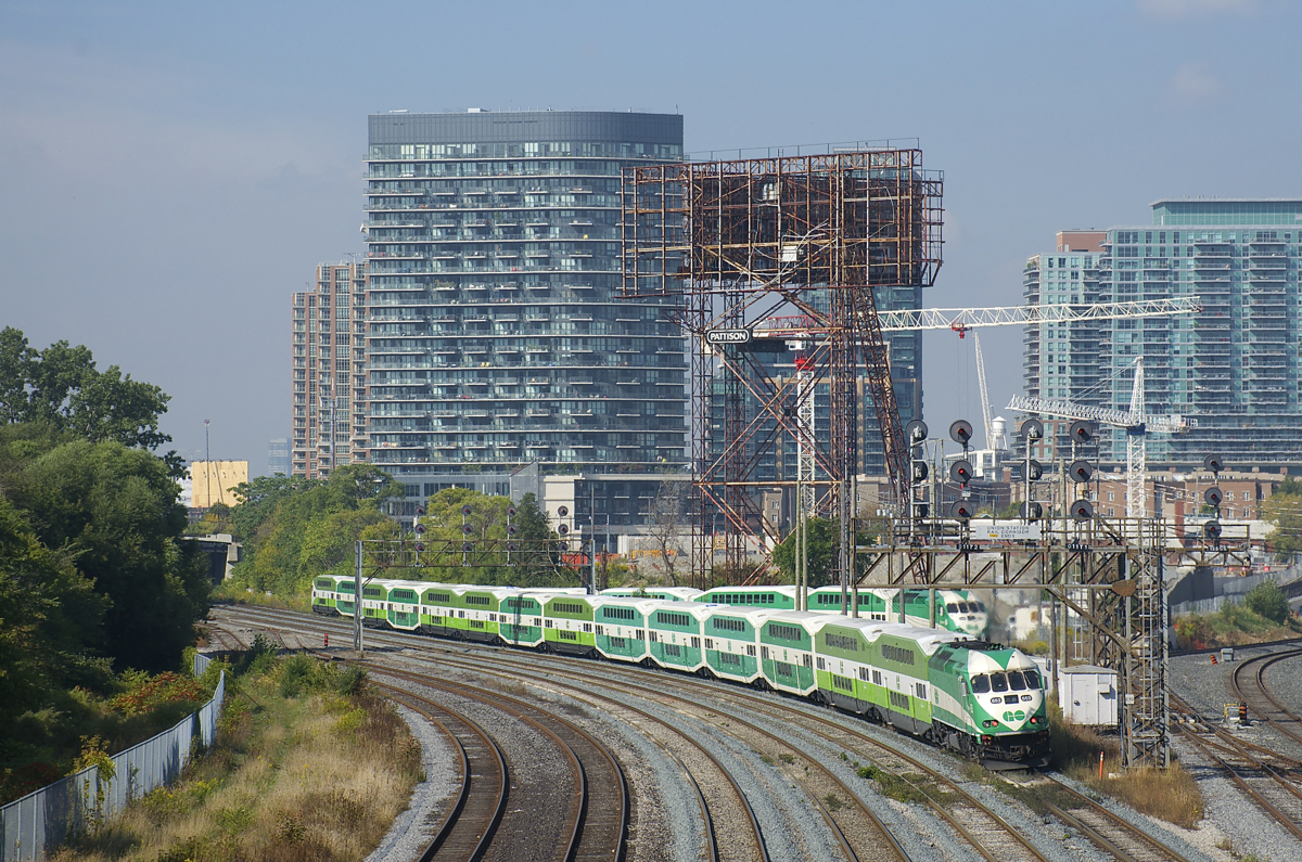 GOT 653 is passing under a number of searchlight signals as it pushes a 12-car train, with a stopped GO train behind it.