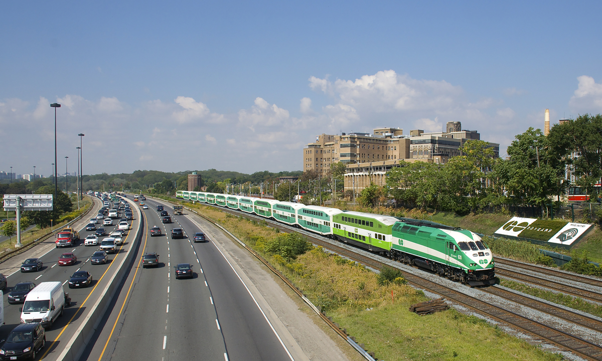A GO Transit eastbound has a car in the new paint scheme at each end, with ten cars in between in the old scheme, as it approaches a pedestrian overpass at MP 4 of the Oakville Sub with GOT 620 leading.
