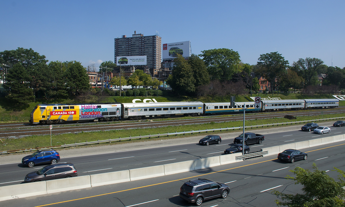 VIA 73 for Windsor is westbound on the Oakville Sub with a slightly unusual consist of three stainless steel cars with a single LRC car second out. Leading is wrapped VIA 906. In the foreground is the the Queen Elizabeth Way highway.