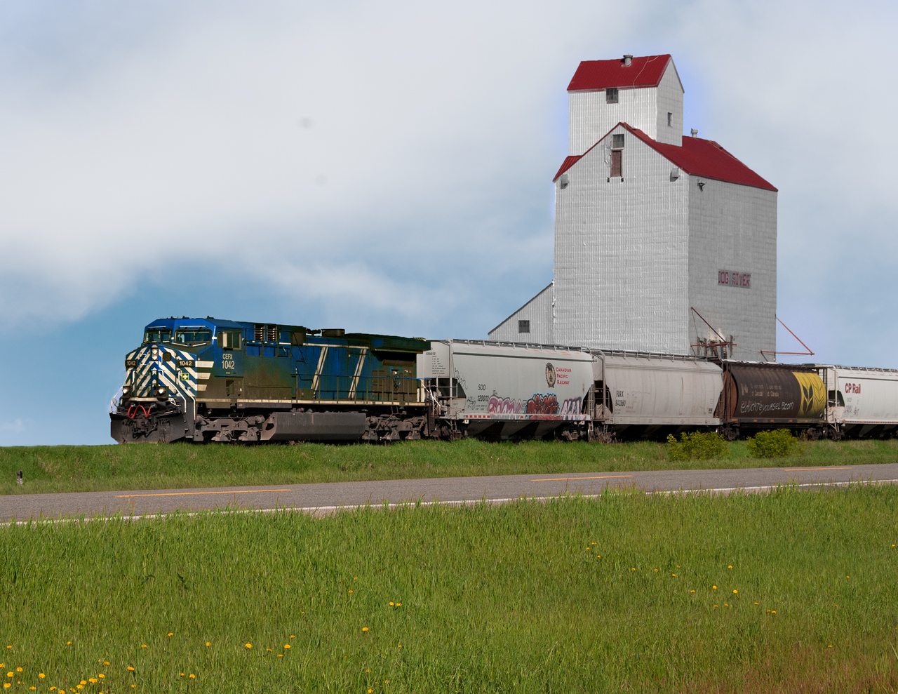 Grain empties from the UP at Kingsgate BC bound for Glenwood MN passes the grain elevator lettered Dog River for the sitcom Corner Gas which was filmed on location here